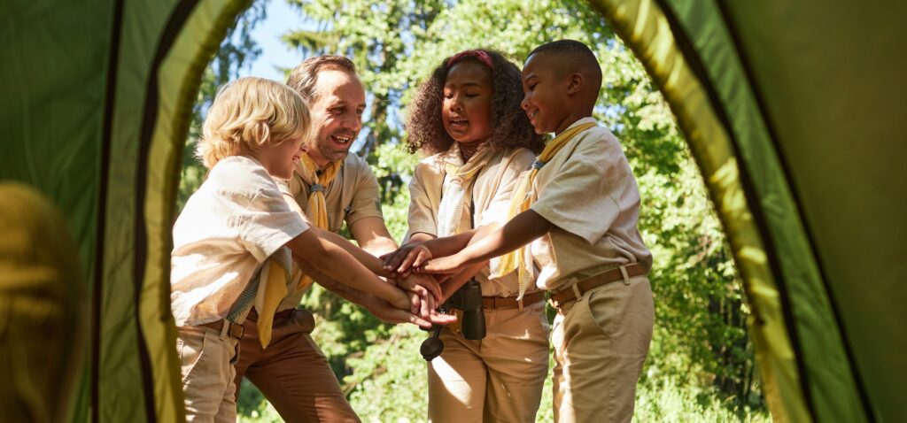 Group of scouts stacking hands and huddling while camping in forest