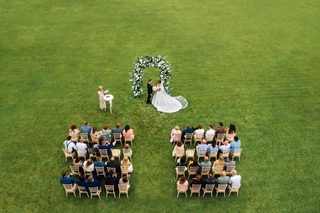 Top view of the Wedding ceremony in a green field with guests sitting on chairs. Wedding venue on